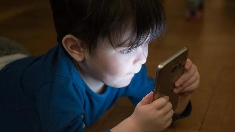 A concerned parent watching a child addicted to a smartphone, highlighting digital safety awareness by Kerala Police.